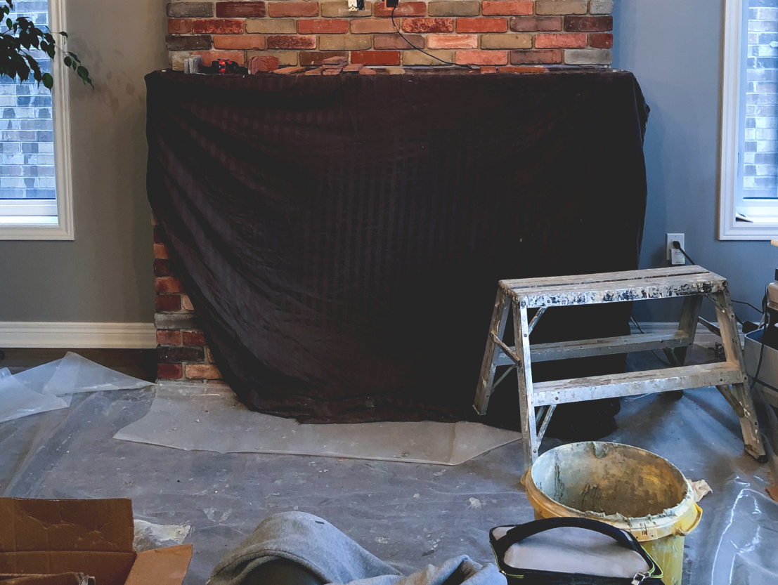 Brick fireplace being converted in living room with black tarp and construction equiptment.